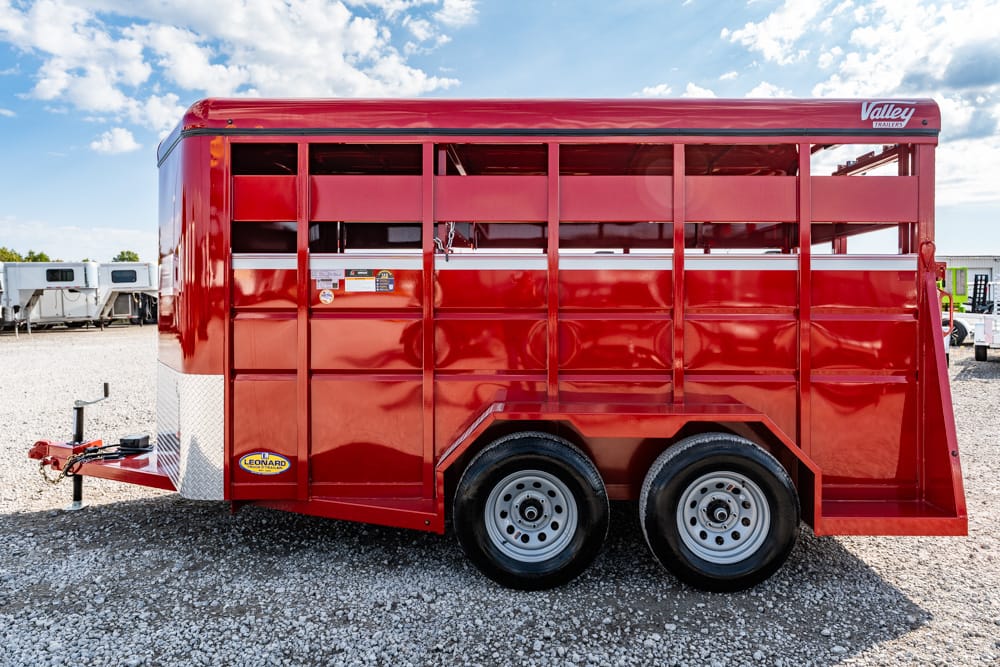 Red livestock trailer with dual wheels and open slat sides parked on a gravel lot; Valley Trailers branding visible on top edge. Readily identifiable as a livestock hauler rather than a person or scene.