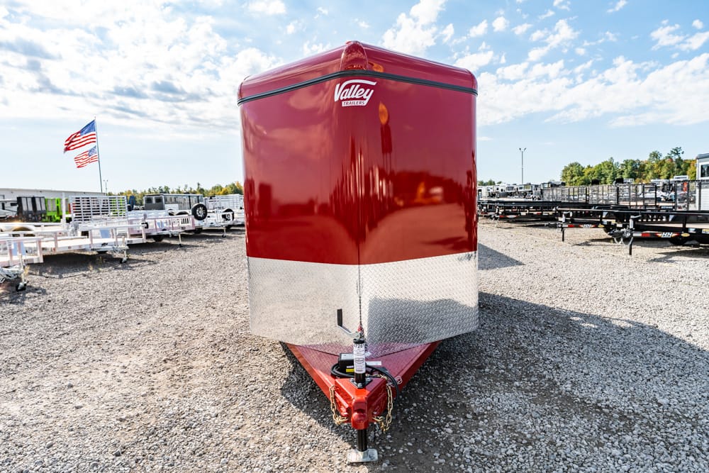 Red, two-tone enclosed trailer with diamond-plate lower panel parked in a lot full of trailers; Valley Trailers logo on top front.
