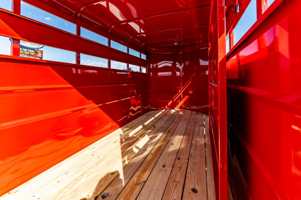 Interior of a bright red trailer with a wooden plank floor, empty and sunlit.