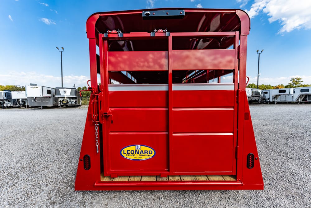 Red livestock trailer with its tailgate open, showing a wooden floor and Leonard brand sticker in a gravel lot with other trailers in the background