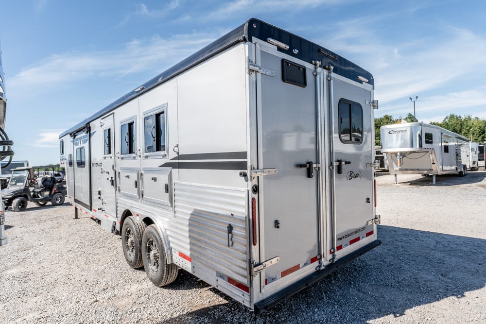 Two‑axle aluminum horse trailer on a gravel lot, with other trailers visible in the background.