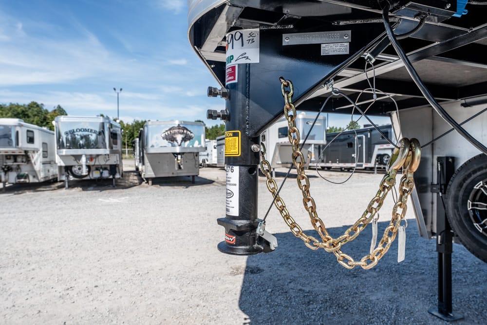 Close-up of a gooseneck trailer hitch with gold safety chains hanging from the tongue, parked in an RV lot.