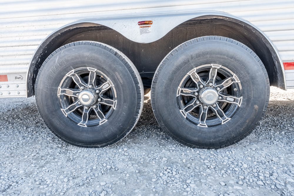 Dual trailer wheels with black rims on a gravel surface