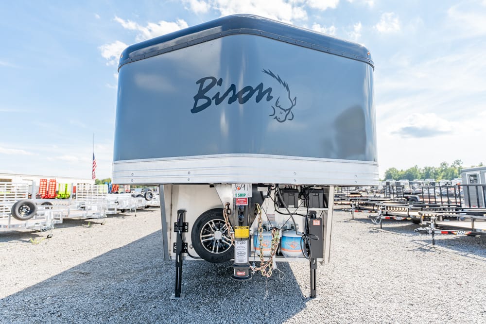 Front view of a blue Bison travel trailer on a hitch, with spare wheel and propane setup visible in a trailer yard.