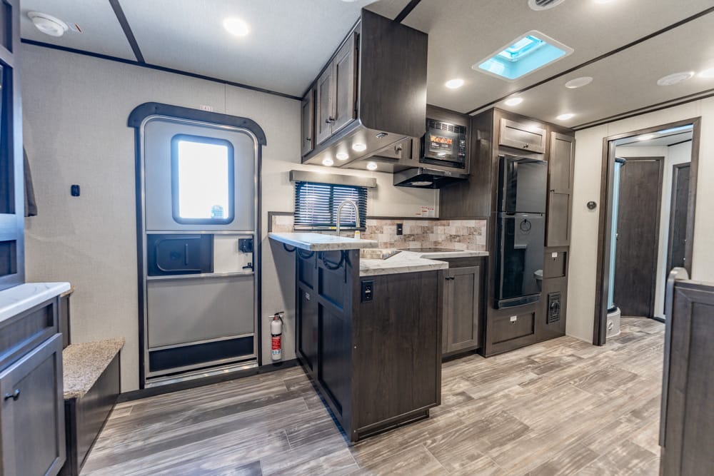 Interior of a modern RV kitchen with a central island, sink, microwave, and dark wood cabinets