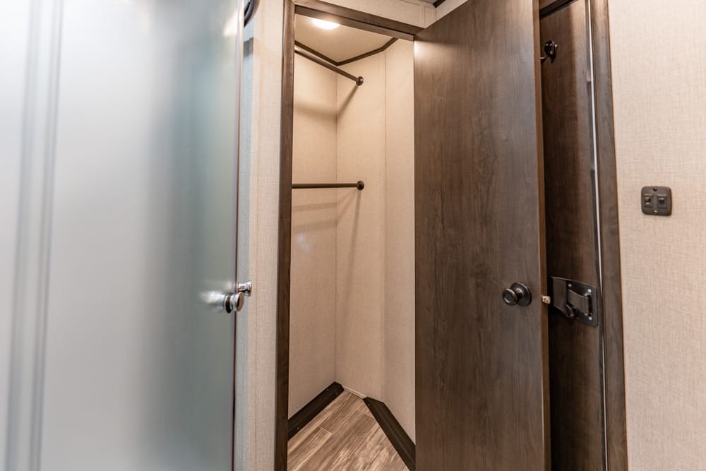 Open closet with two hanging rods inside a compact alcove, dark wood door framing