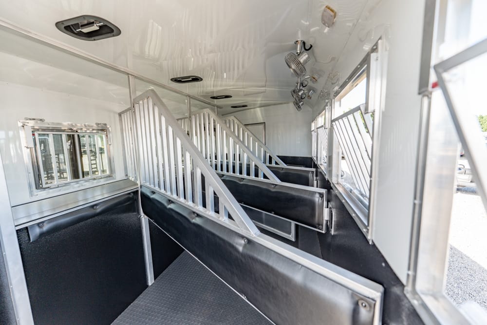 Interior of a horse trailer with partitioned stalls, metal rails, and padded black walls for horses.