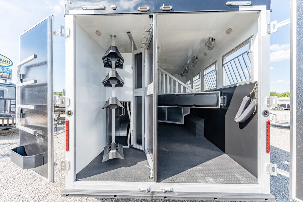 Interior of an empty horse trailer with stalls, a raised divider, and tack racks along the left wall for equipment storage on the go at a stable yard