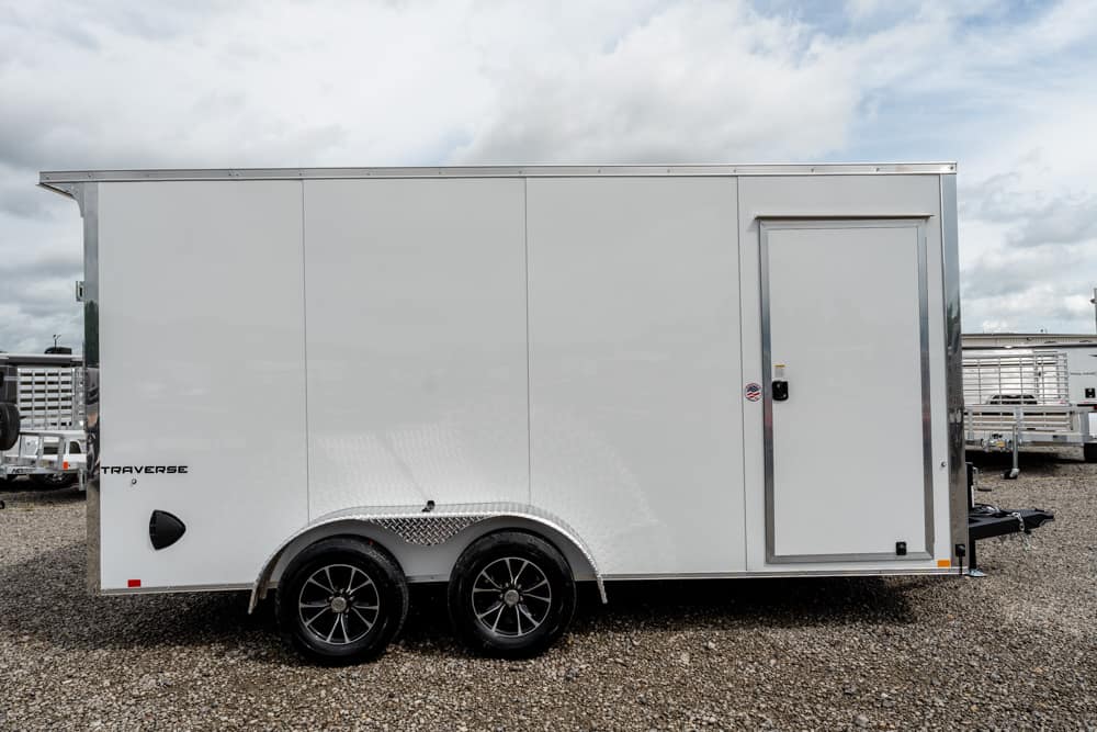 White enclosed cargo trailer with dual axles and a side access door on a gravel lot.