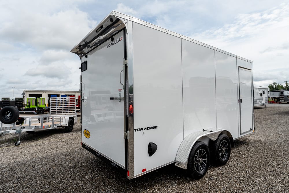 White enclosed cargo trailer with dual axles and diamond-plate fenders parked on a gravel lot.