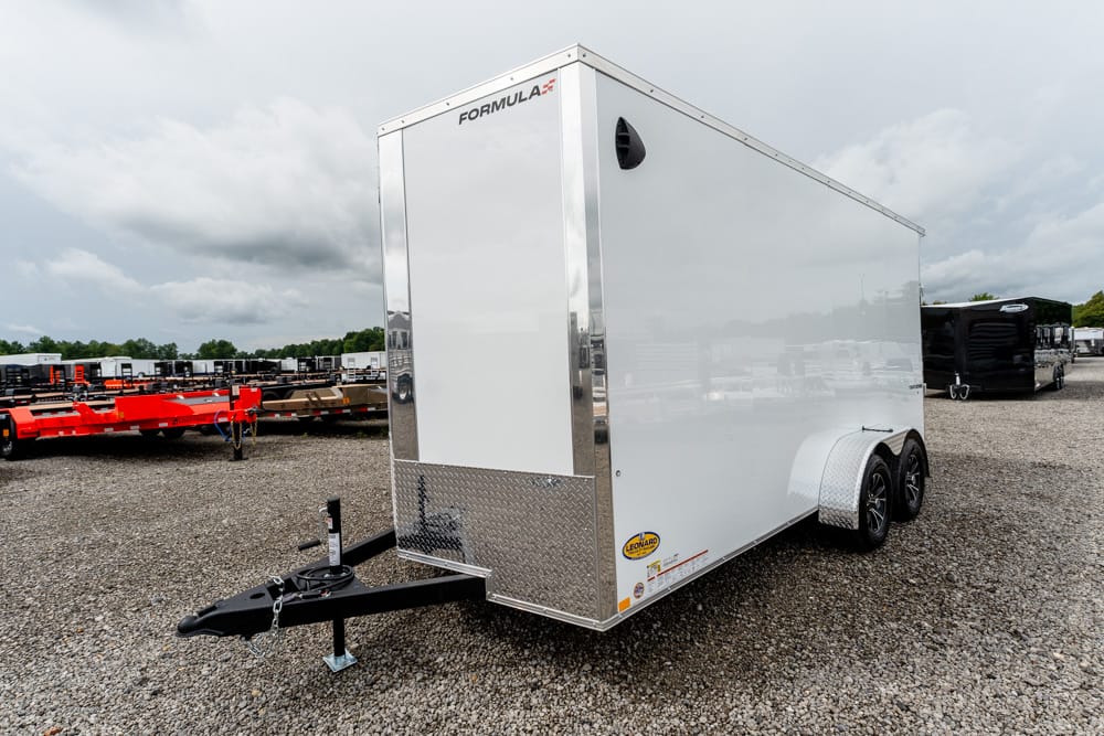 White enclosed cargo trailer with chrome trim and dual axles on a gravel lot, front view showing hitch. **NOTE:** brand 'FORMULA' near the top edge.