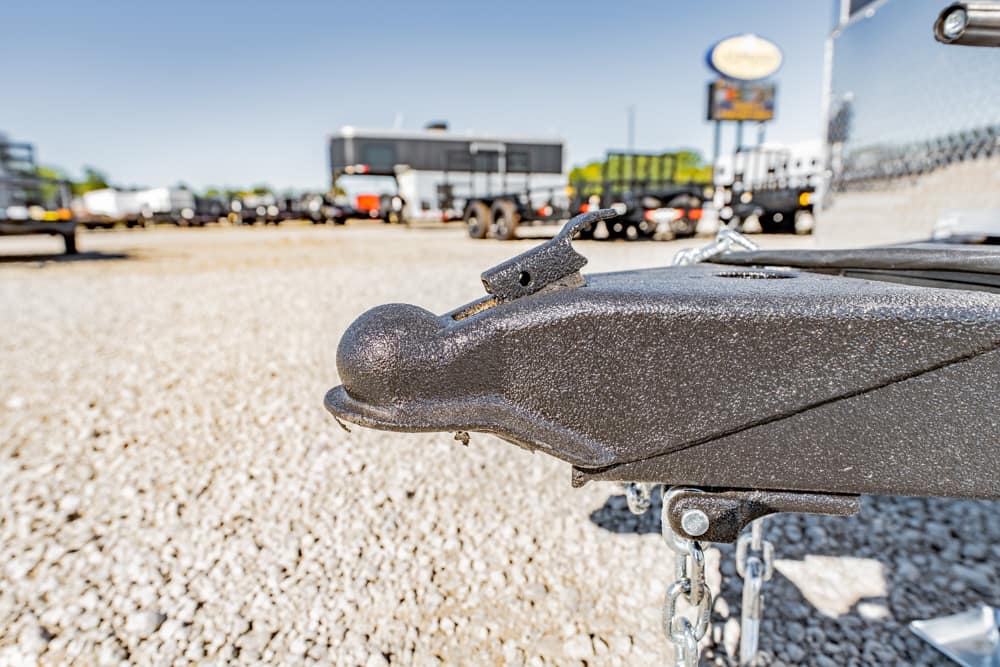 Close-up of a metal trailer hitch ball on a gravel lot, with chains and a blurred line of trailers in the background
