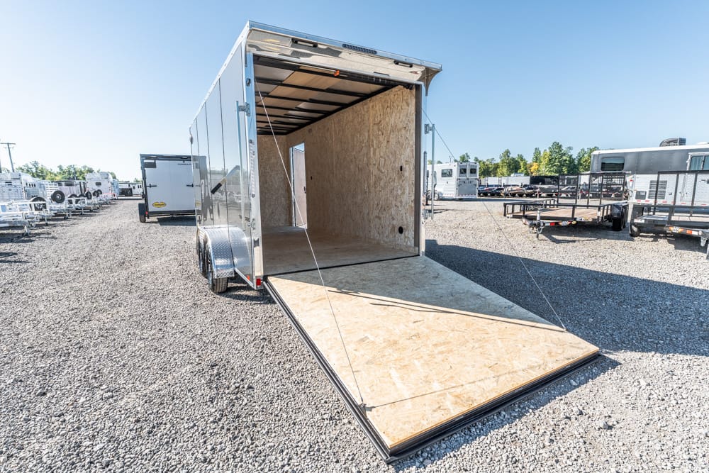 Enclosed cargo trailer with its wooden ramp lowered in a gravel lot, ready for loading.