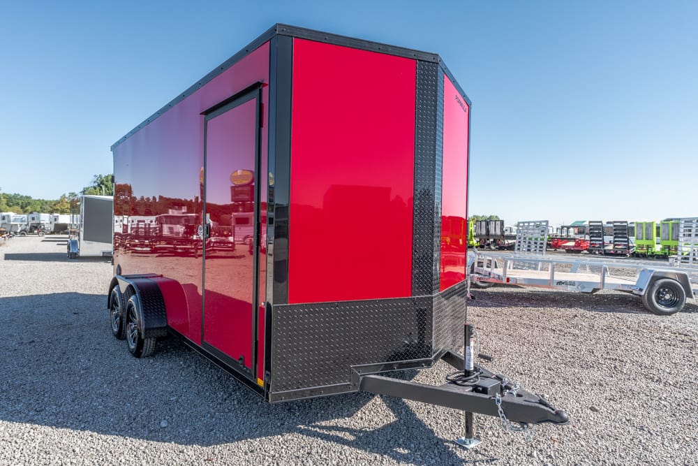 Red enclosed cargo trailer with black trim and diamond-plate front, on a gravel lot with a hitch in the foreground.
