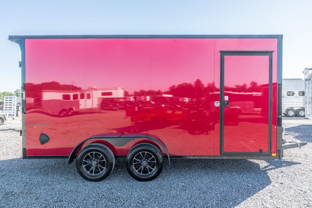 Red enclosed cargo trailer with two axles on a gravel lot, side door visible and black trim.
