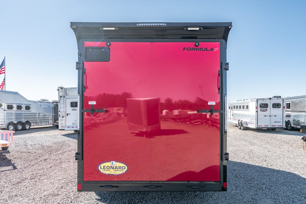 Rear view of a bright red Formula horse trailer with a black frame, Leonard logo on the lower left, in a gravel trailer lot.