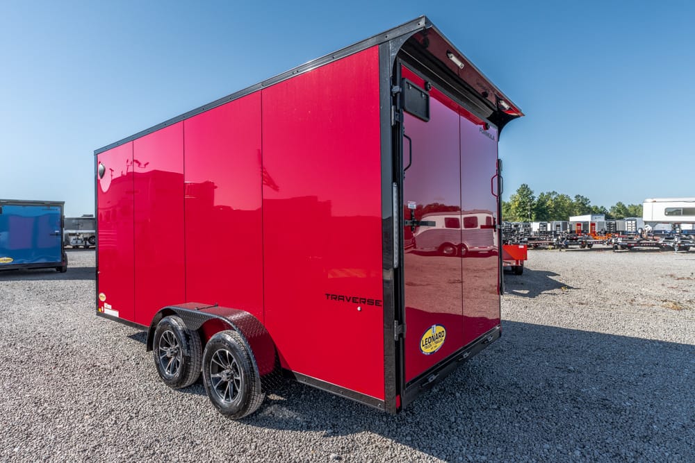 Red enclosed cargo trailer with dual axles and black fenders on a gravel lot.