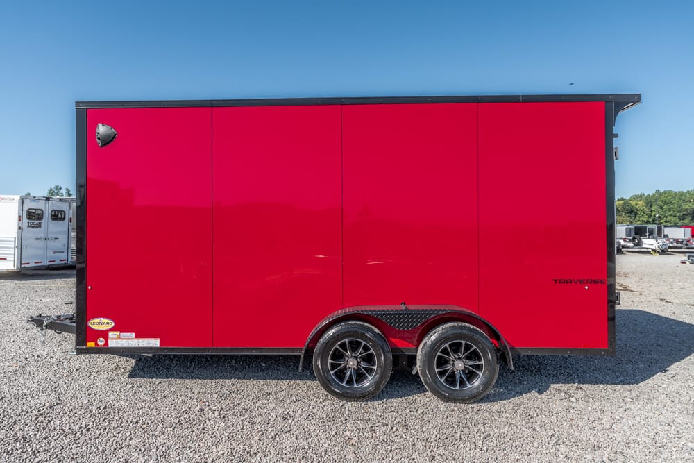 Red enclosed cargo trailer with black frame and dual-axle wheels parked on gravel lot.