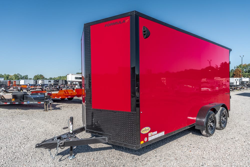 Red enclosed, dual-axle cargo trailer with black diamond-plate front and fenders, hitched on a gravel lot, Formula branding on the top edge
