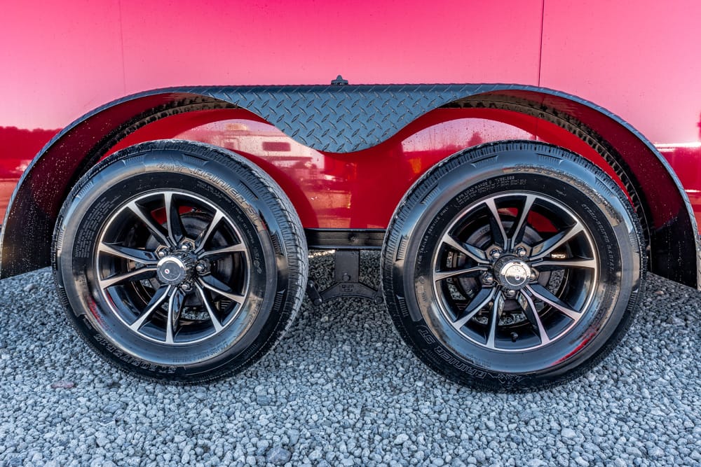 Dual wheels on a red trailer with a diamond-plate fender, resting on gravel.