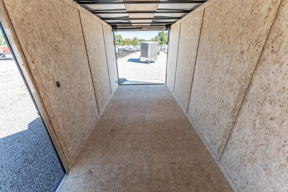 Interior of an empty plywood-sided trailer, looking toward the open back on a sunny day in a gravel lot