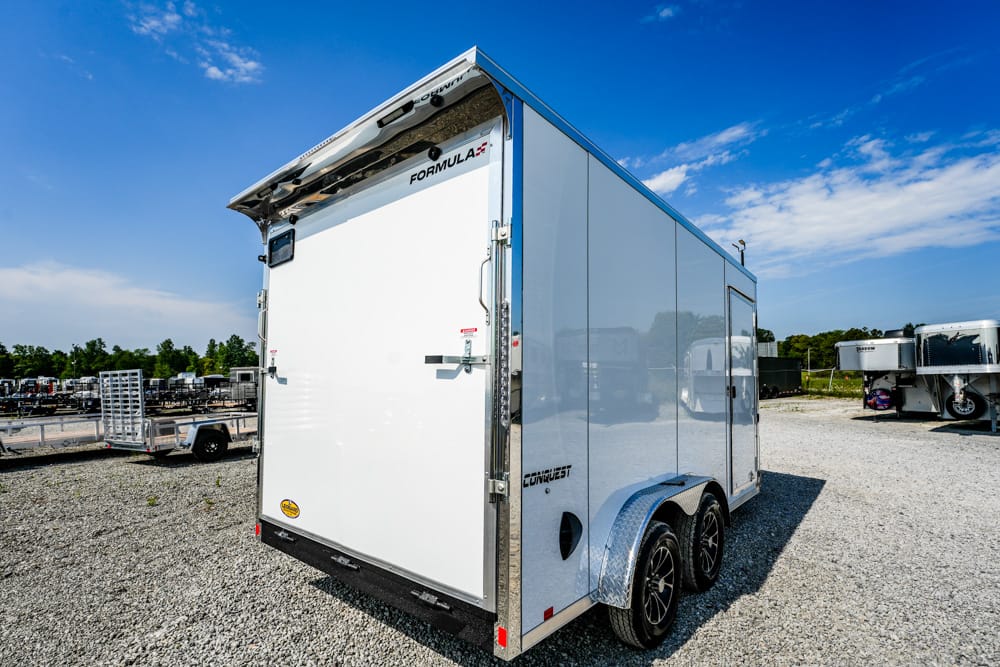 White enclosed dual-axle cargo trailer with a back ramp door on a gravel lot.