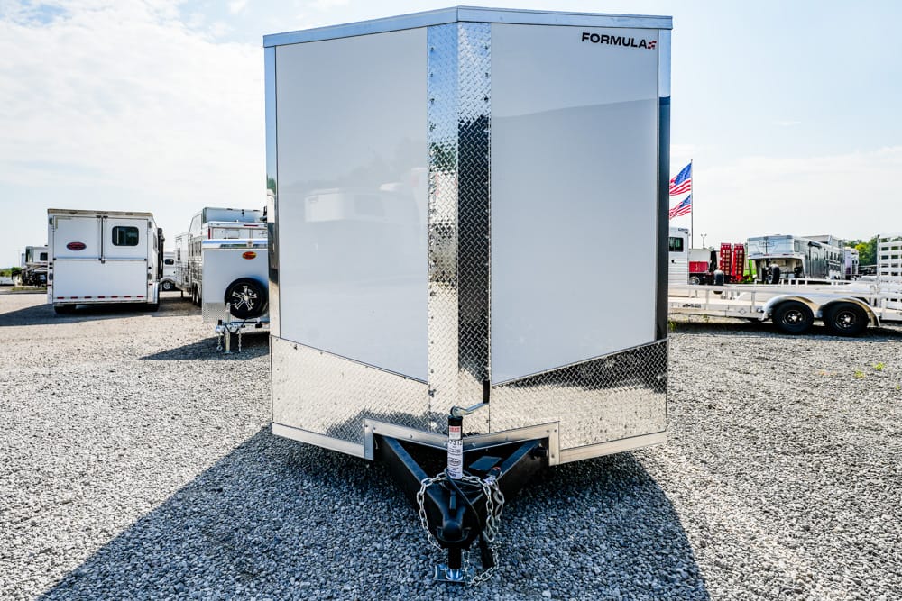 Enclosed white cargo trailer with chrome diamond plate trim and hitch in a gravel trailer yard.