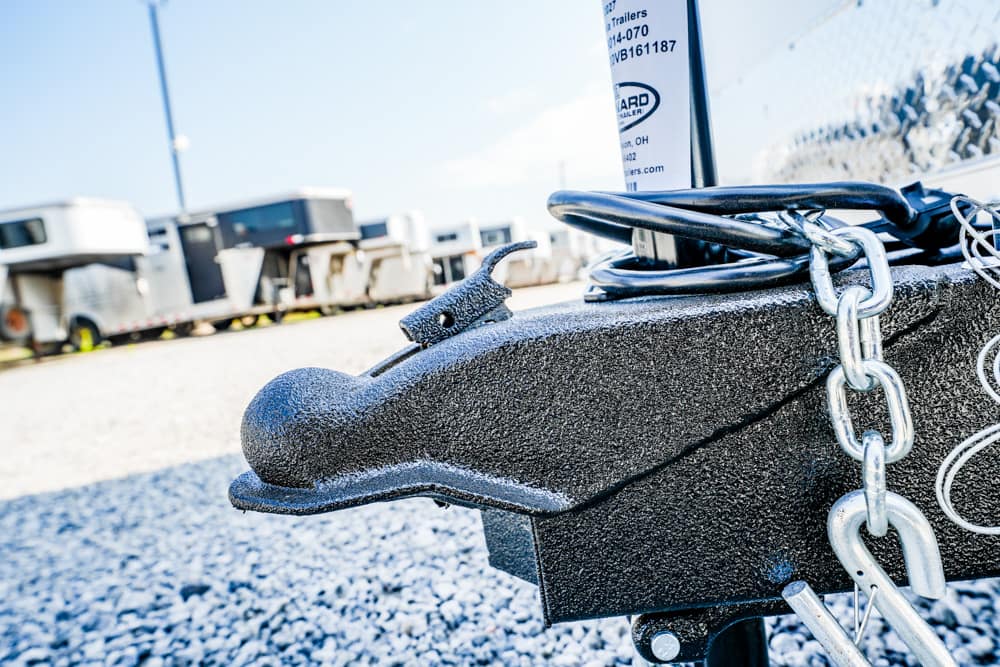 Trailer hitch with a heavy chain and padlock secured to a trailer in a gravel lot, with other trailers in the background