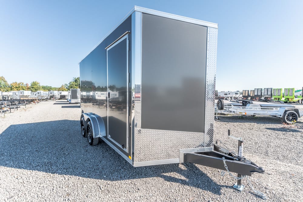 Enclosed dual-axle cargo trailer on a gravel lot with a front hitch and diamond-plate trim.