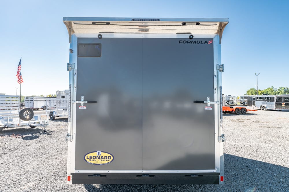 Back of a grey Formula trailer with a Leonard logo at bottom left, in a large outdoor lot with other trailers nearby.
