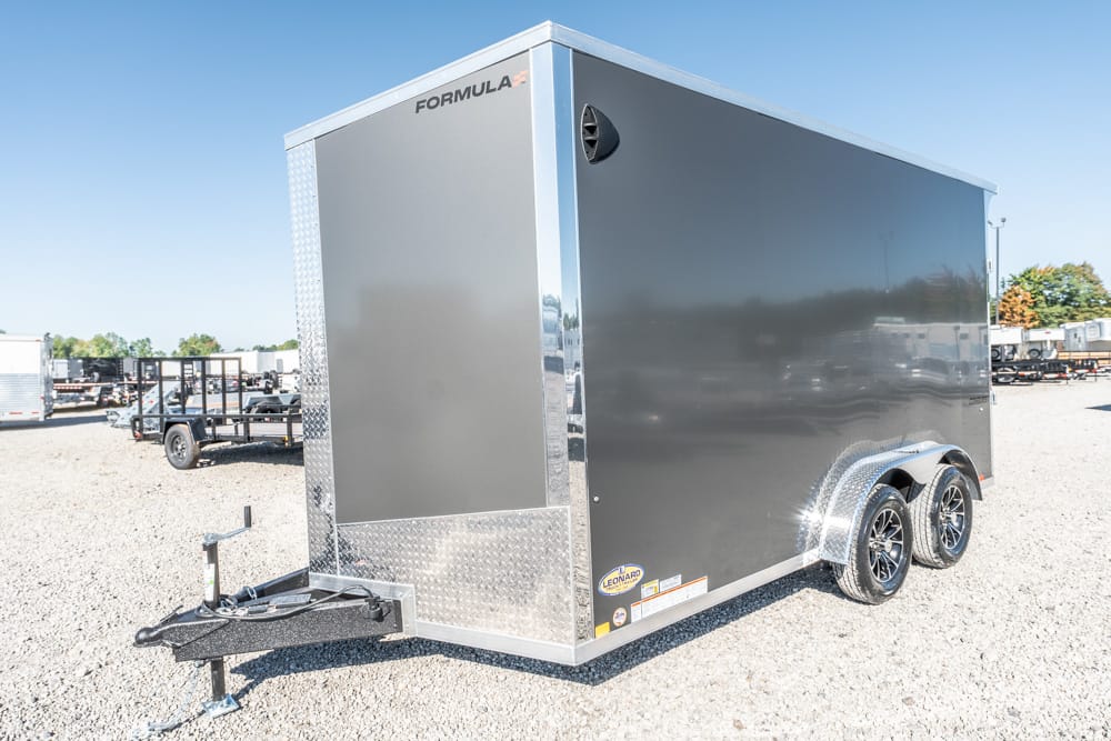 Enclosed gray utility trailer with dual axles and diamond plate trim on a gravel lot; hitch and front jack visible.
