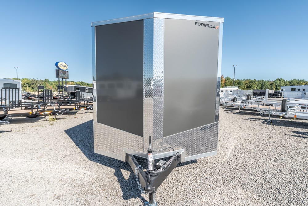 Enclosed gray Formula trailer with diamond plate trim parked on a gravel lot, hitch and jack visible at the front.