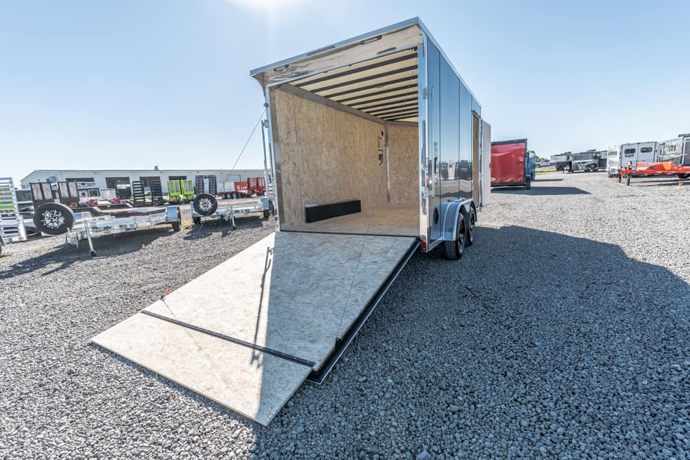 Open cargo trailer with a ramp down, parked on a gravel lot with other trailers in the background.