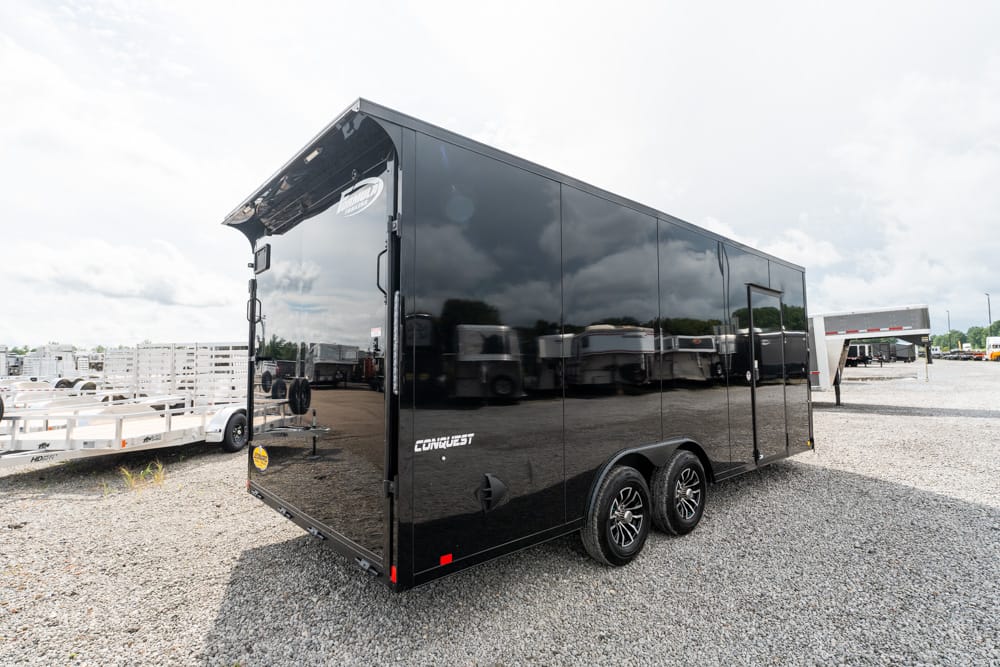 Black enclosed cargo trailer with dual axles parked on a gravel lot in a trailer yard.