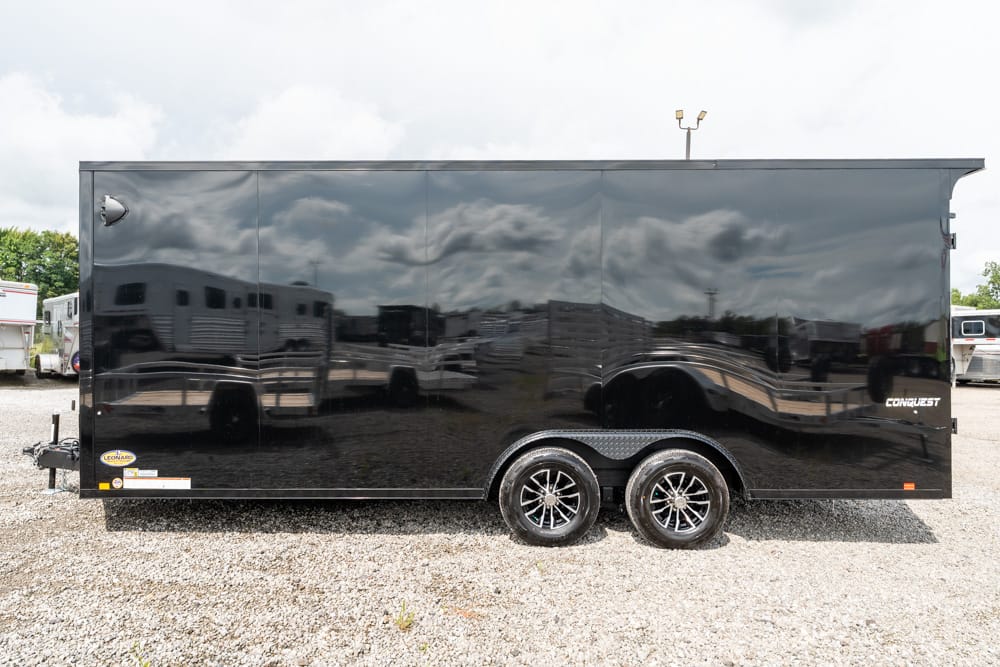 Black enclosed cargo trailer with dual axles and chrome rims, parked on a gravel lot; Conquest branding along the side.