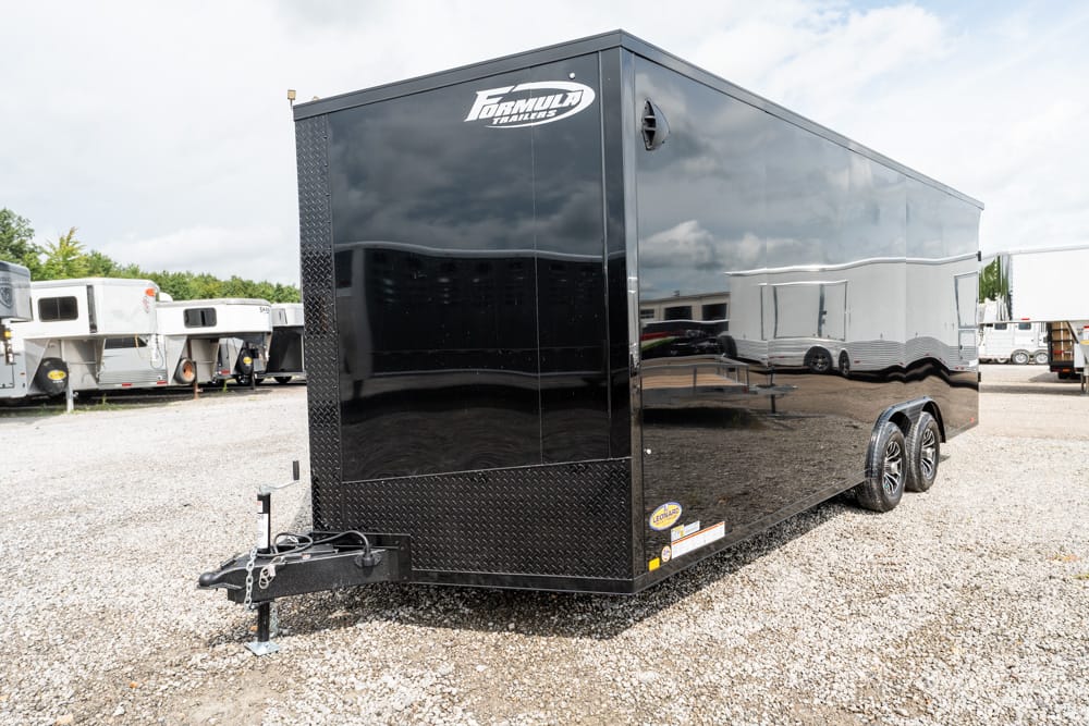 Black enclosed dual-axle cargo trailer on a gravel lot, with a diamond-plate front and a hitch at the front, Formula Trailers logo on top corner.