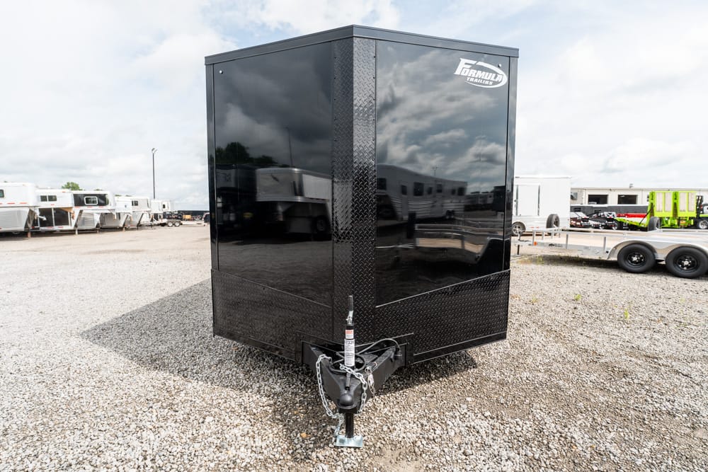 Black enclosed cargo trailer in a gravel lot, hitch and safety chains visible at the front.