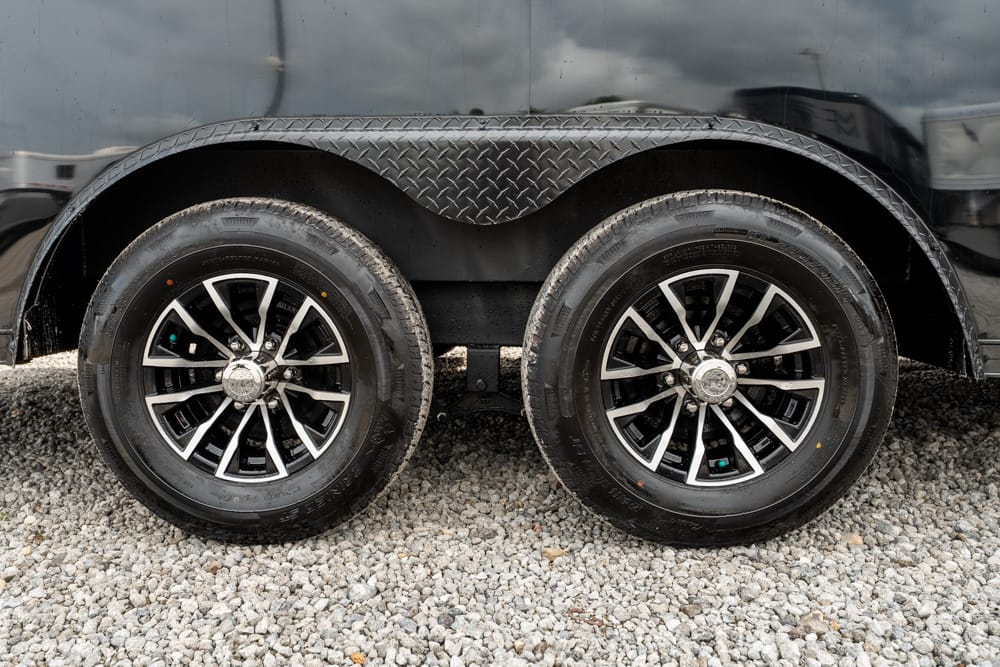 Dual-axle trailer wheels with diamond-plate fender on a gravel surface.
