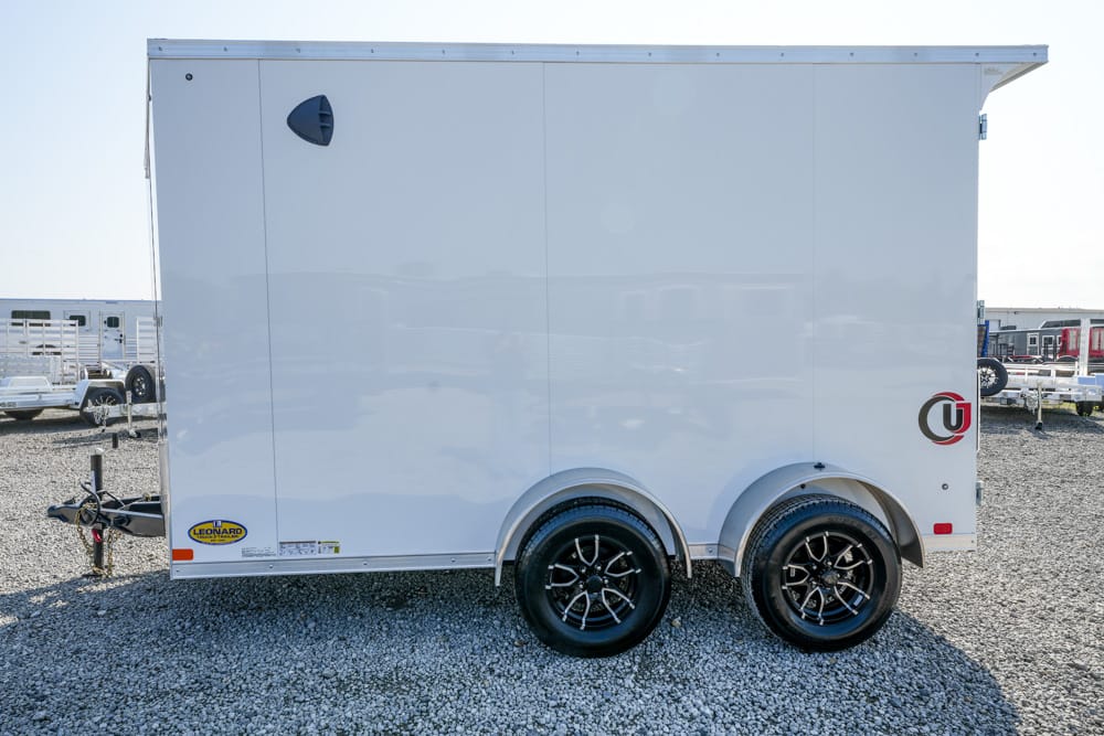 White enclosed utility trailer on a gravel lot, dual axles with black rims.