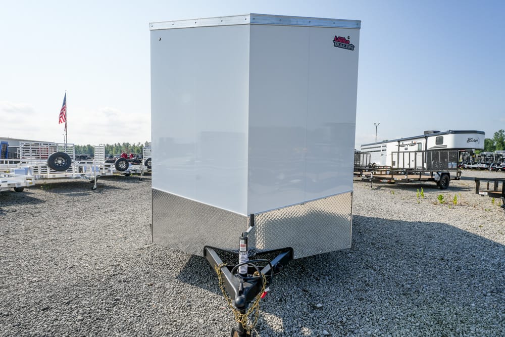 Tall white enclosed trailer with diamond-plate front on a gravel lot; hitch and propane tank visible, other trailers in background.