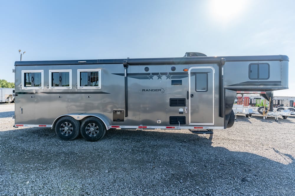 Silver gooseneck horse trailer with living quarters, four side windows, double-axle wheels, and RANGER branding on gravel lot.