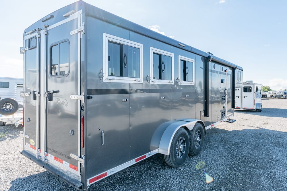 Long gray two-axle horse trailer with side windows parked on a gravel lot.