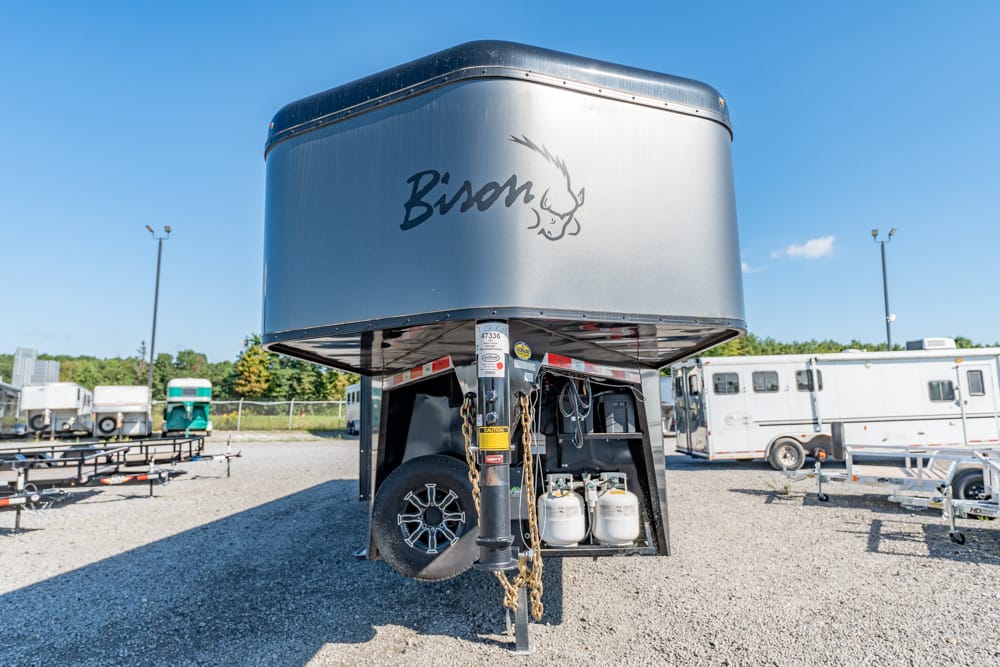 Silver Bison gooseneck trailer parked in a gravel lot, with chains, hitch, and propane tanks visible at the front.