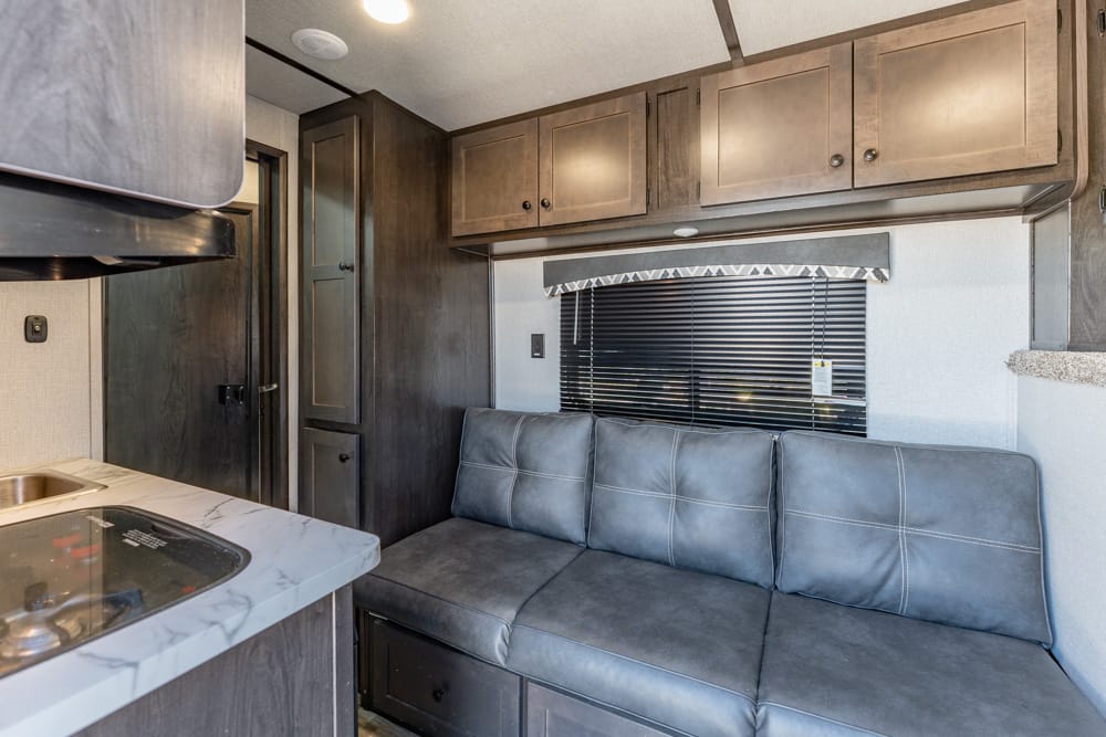 RV living area with dark wood cabinets, a gray leather sofa, and a window with blinds above the seating area
