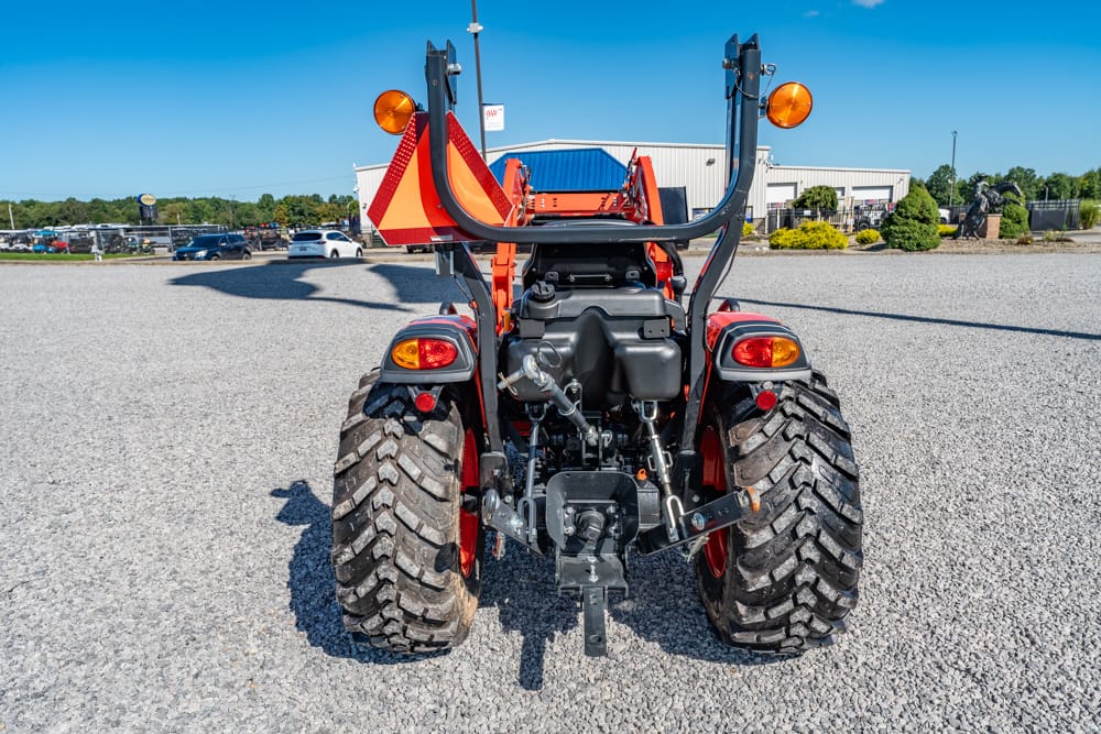 Rear view of a red tractor with oversized mud tires, hydraulic system, and a slow‑moving vehicle sign mounted on the back.