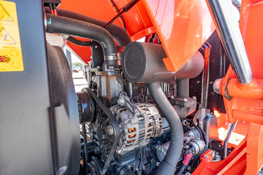 Close-up view of an orange industrial engine showing belts, pulleys, hoses, and an alternator.