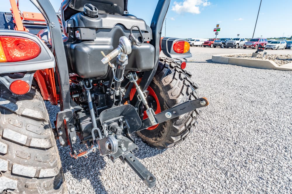 Rear view of a red tractor showing hydraulic hitch components and a large off-road tire on a gravel parking lot