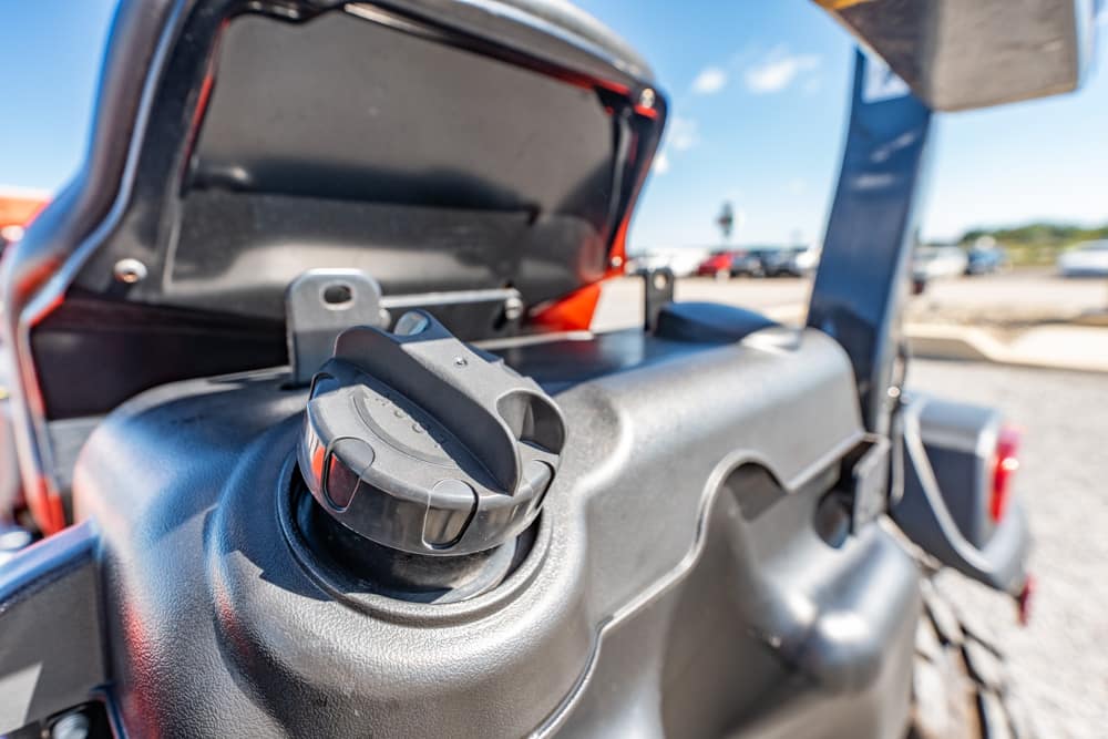 Close-up of a black fuel cap on a rugged jeep with the rear hatch open in a sunny parking lot.