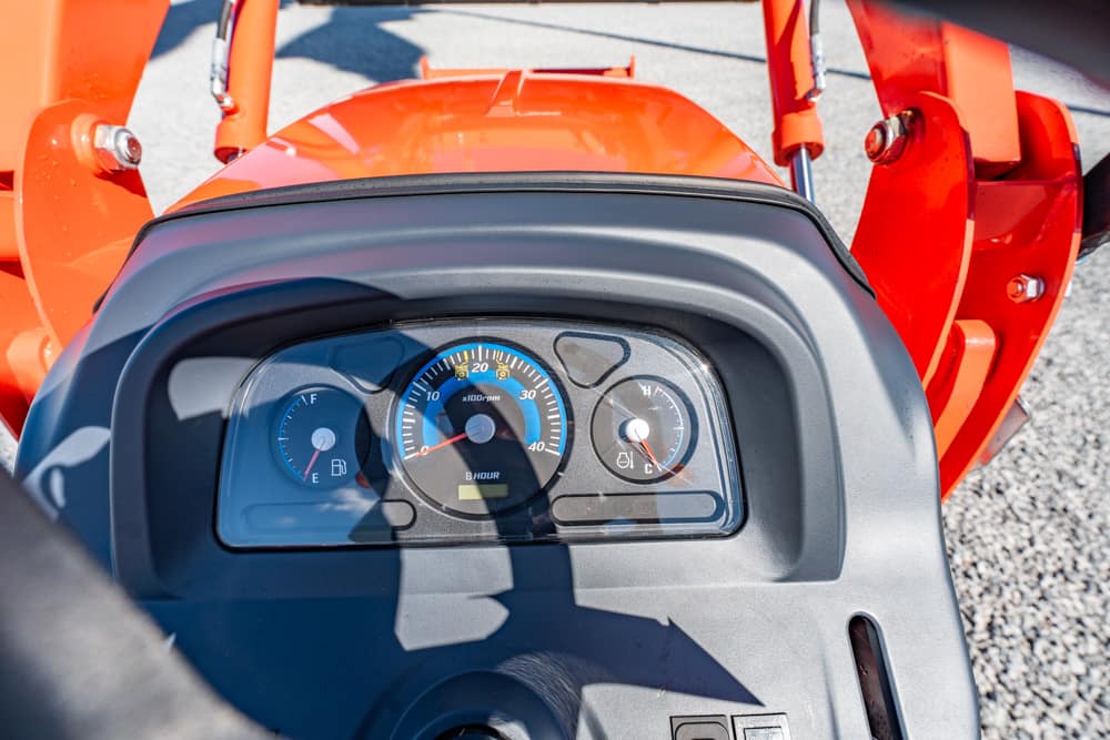 Dashboard of an orange tractor showing tachometer, fuel gauge, and hour meter within the cockpit area (close-up).