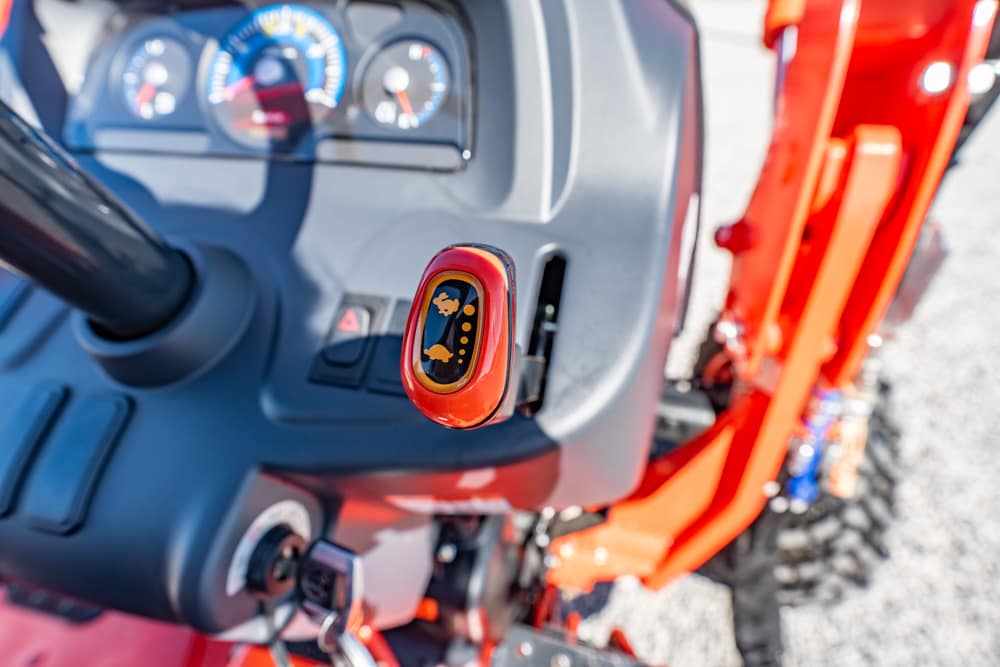 Close-up of a red tractor control lever inside the cockpit, with gauges visible behind it in the dashboard area.